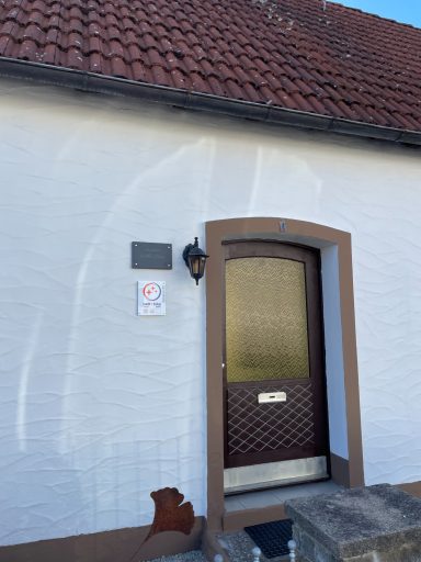 Haustür mit braunem Rahmen, weißer Wand und Ziegelstein-Dach. Zwei Schilder: Villa Rosa auf einer Schiefertafel und ein Bett + Bike Logo.