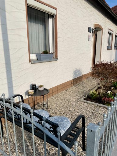 Sitzbereich mit Stühlen und Tisch vor einem weissen Haus, umgeben von Blumenbeeten.